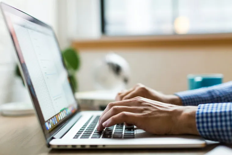 Mains qui tapent sur le clavier d'un ordinateur portable posé sur un bureau en bois