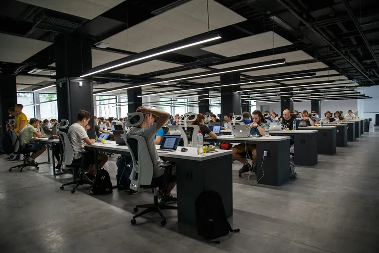 Grand open space avec des rangées de bureaux où travaillent de nombreuses personnes sur ordinateur portable