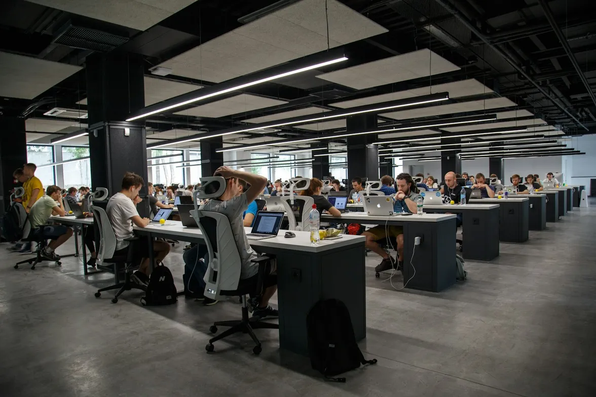 Grand open space avec des rangées de bureaux où travaillent de nombreuses personnes sur ordinateur portable