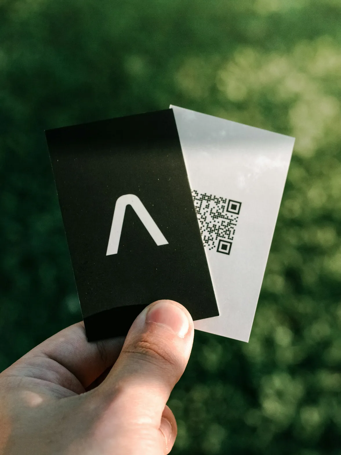 Main tenant deux cartes de visite, l'une noire avec un logo, l'autre blanche avec un QR code